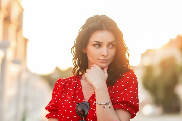 Elegant beautiful italian girl in a fashionable red dress with a stylish silver bracelet on her arm is walking in the city