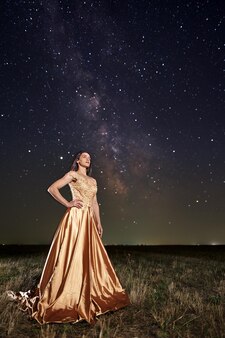 Bella donna elegante in un vestito lungo sotto il cielo notturno della via lattea