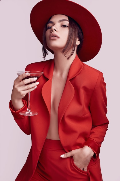 Elegant beautiful woman in a red fashionable suit and hat with cocktail