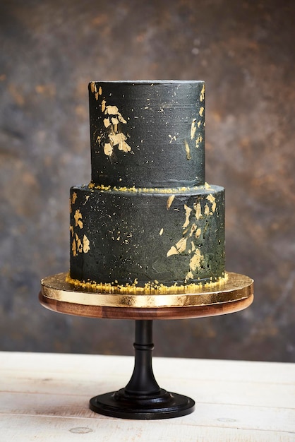 Foto elegante torta nuziale nera e oro dall'aspetto moderno e lussuoso, adagiata su una base in legno, ha un aspetto marmorizzato, realizzata in crema al burro e foglia d'oro.