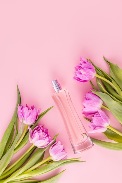 Foto elegante bottiglia di profumo rosa tra i tulipani su sfondo rosa vista superiore presentazione piatta di una fragranza modello di bottiglia vuota vista verticale