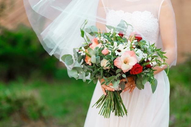 Elegant bride in a wedding dress with lace and veil holding bridal bouquet of flowers