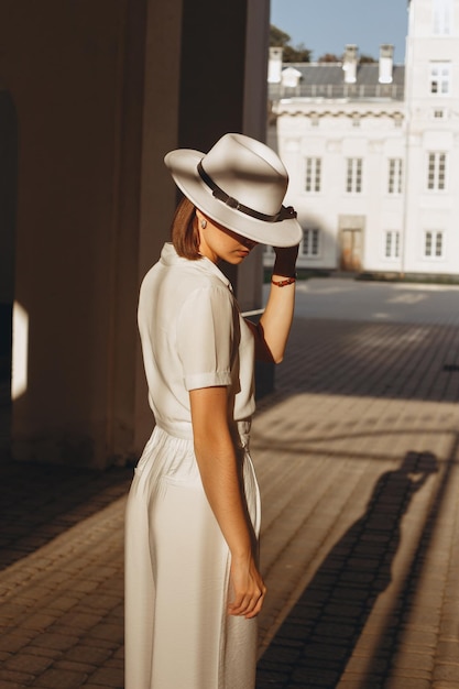 elegant bride in white blouse and pants covering face with hat