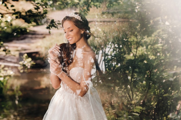 An elegant bride in a white dress, gloves with a bouquet on a waterfall in the Park, enjoying nature.Model in a wedding dress and gloves in the forest.Belarus