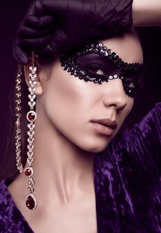 Elegante donna bruna in un bellissimo vestito viola, maschera di paillettes e guanti neri
