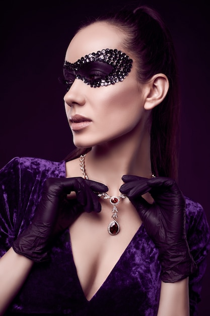 Elegante donna bruna in un bellissimo vestito viola, maschera di paillettes e guanti neri