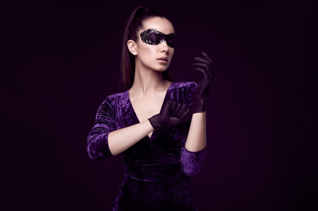 Elegant brunette woman in beautiful purple dress and sequins mask glove up