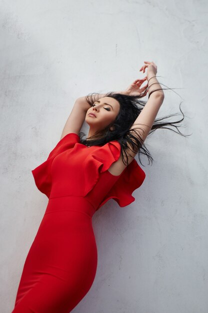 Elegant brunette woman in red dress stands near the walls