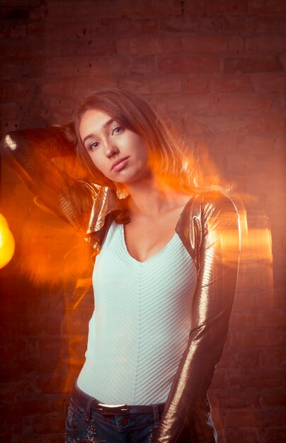 Elegant  brunette woman in shiny gold jacket and blue jeans. Mixed lighting photography