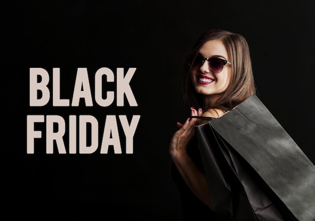 Elegant brunette woman wears sunglasses and black dress holding black shopping bags black friday concept