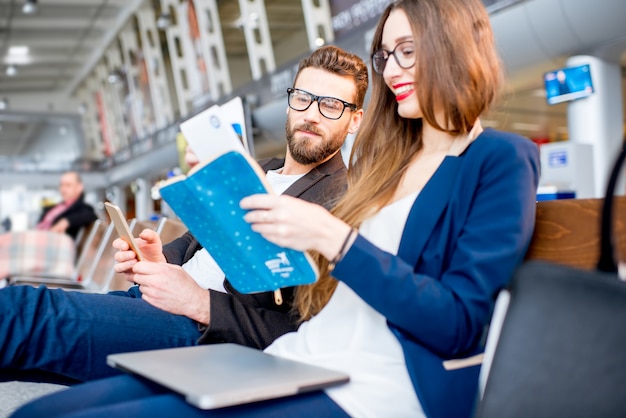 Elegant business couple looking on the airplane tickets at the waiting hall in the airport. Business travel concept