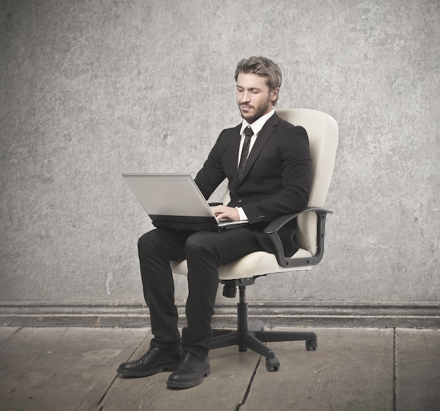 Элегантный бизнесмен сидит в кресле с ноутбуком
