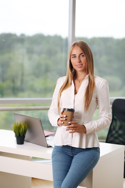 Donna di affari elegante nel suo ufficio che tiene una tazza di caffè