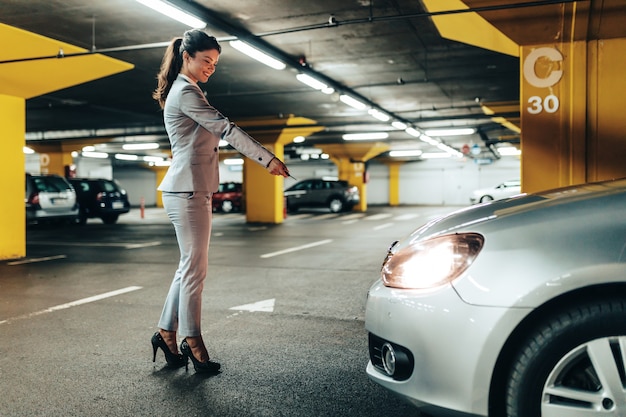 Elegant businesswoman locking her car with keys in underground parking.