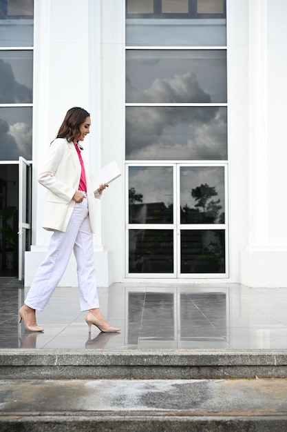 Elegant businesswoman or manager in white formal suit walking along the building