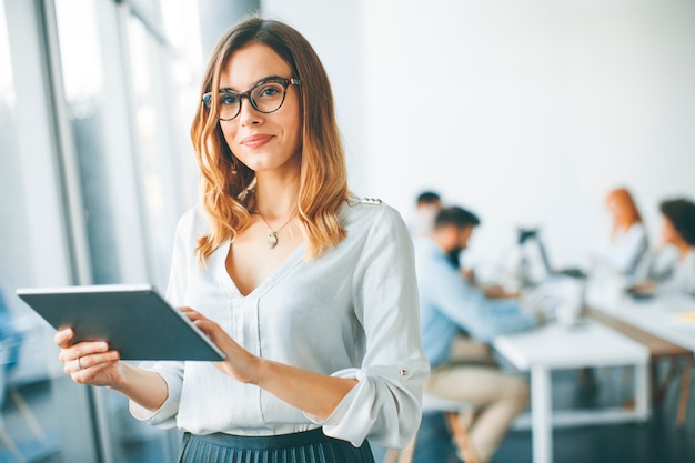 Foto donna di affari elegante che sta nell'ufficio con la compressa digitale