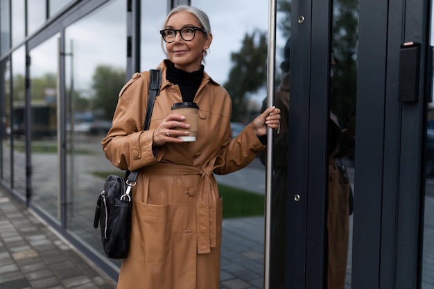 Элегантная кавказская деловая женщина средних лет с чашкой кофе входит в офисное здание