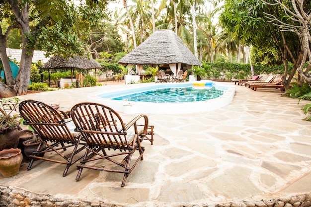 Elegant chairs made of wood close to a swimming pool inside a Kenyan garden