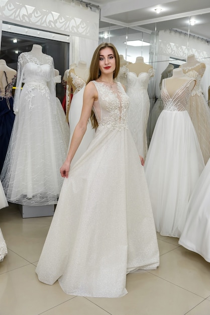 Elegant cheerful lady in bridal dress standing in wedding salon