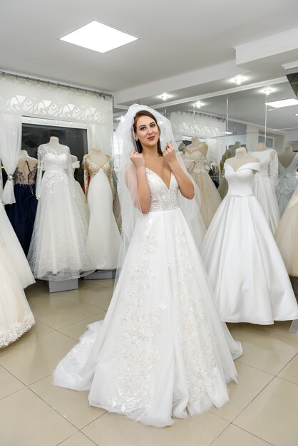 Elegant cheerful lady in bridal dress standing in wedding salon