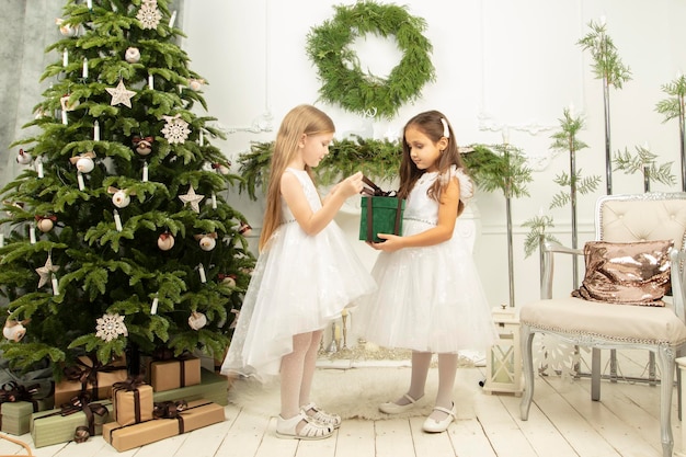 Elegant children at the Christmas tree Two little girls in christmas with a gift