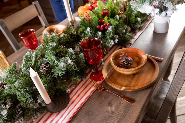 Elegant Christmas dinner table setting Decoration of Christmas table candles juniper branches and napkins wooden plates New Year decorations in living roomcountry style