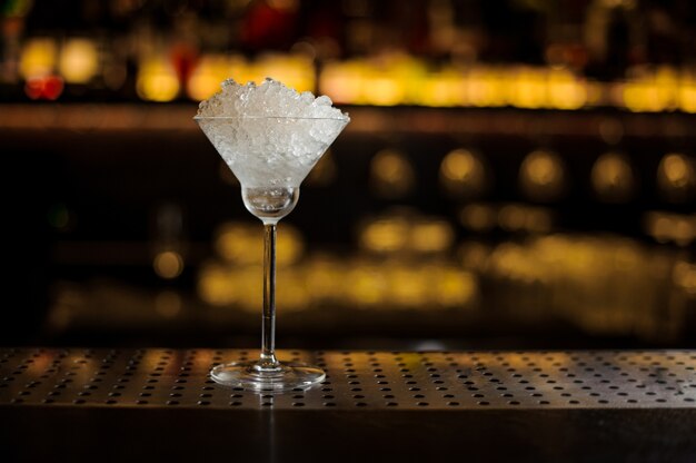 Elegant cocktail glass filled with a lot of ice pieces on the bar counter against the lights