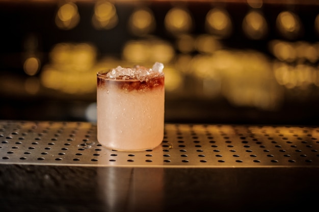 Elegant cocktail glass filled with tasty sweet alcoholic drink with ice on the bar counter