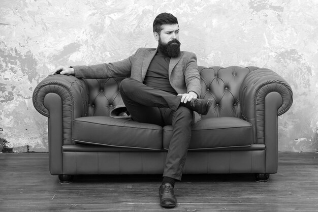 Elegant and confident Man of fashion Fashion model relaxing on sofa Bearded man enjoying casual fashion style Fashionable businessman Business and fashion