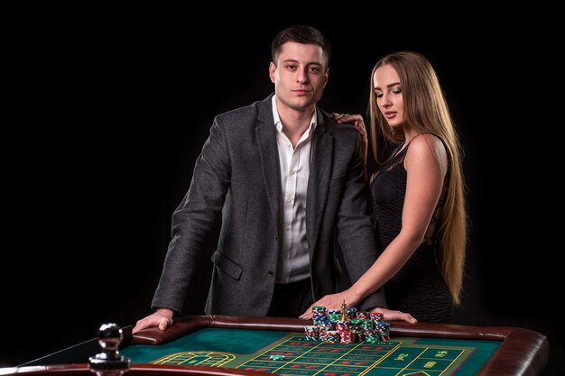 Elegant couple at the casino betting on the roulette, on a black background