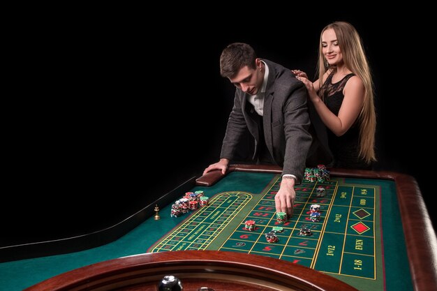 Элегантная пара в казино, делая ставки на рулетку, на черном фоне