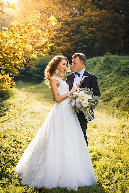 Elegant curly bride and stylish groom hugging on the green meadow