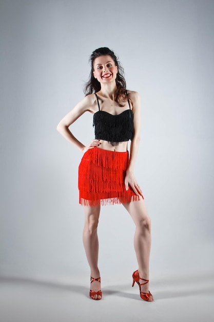 An elegant dancer performs a Latin American dance in an elegant red dress with sparkling jewelry Fashion and beauty Ballet show Studio portrait