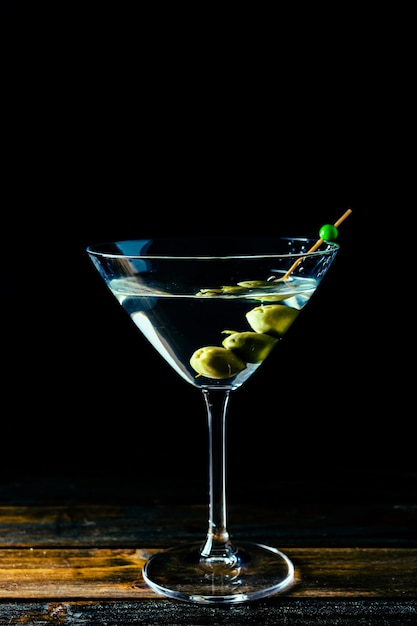 Un elegante bicchiere da martini secco con olive spruzzate su sfondo nero con spazio per la copia. orientamento verticale.