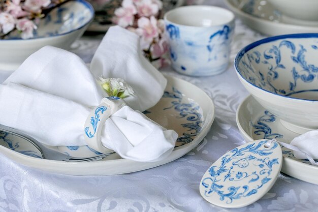 Elegant Easter table setting with empty marine ornament painted porcelain tableware plates and bowls Easter eggs decorations on white tablecloth Easter holiday dinner