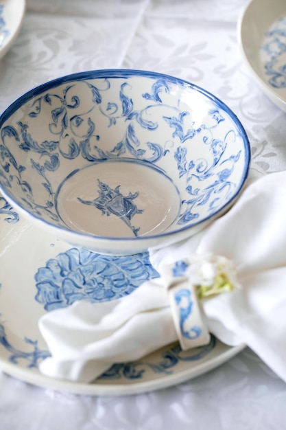 Elegant Easter table setting with empty marine ornament painted porcelain tableware plates and bowls on white tablecloth Easter holiday dinner Close up