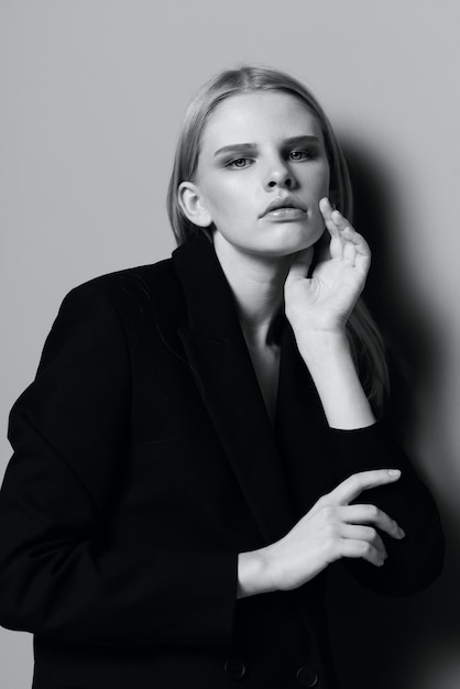 Elegant girl puts her hand to her face tucks her hair behind her ear poses in the studio in black and white style