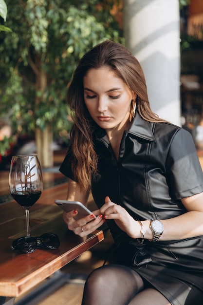 Elegant and glamour beautiful woman in black latex dress with smartphone in restaurant.