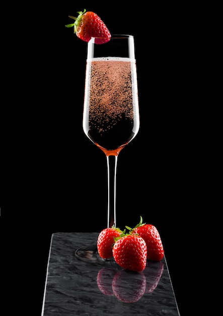 Elegant glas roze roze champagne met aardbei op de top en verse bessen op zwart marmeren bord op zwart.