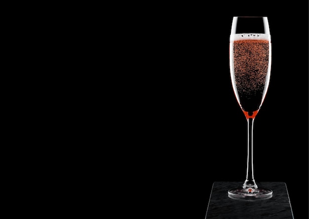 Elegante bicchiere di champagne rosa rosa con bollicine su tavola di marmo nero su fondo nero