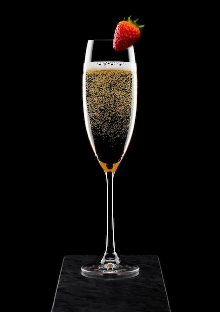 Elegant glass of yellow champagne with strawberry on top on black marble board on black