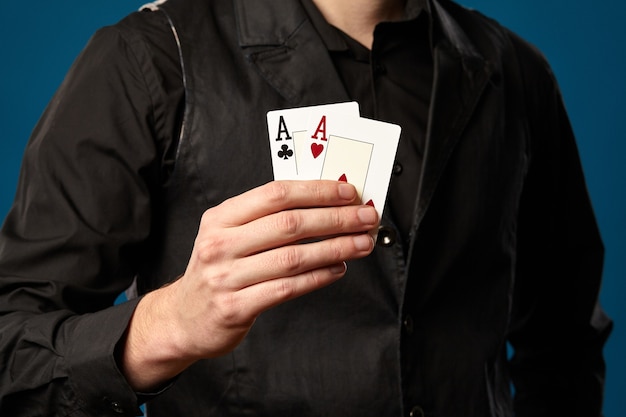 Elegant guy, newbie in poker, in black vest and shirt. Holding two playing cards, aces, while posing