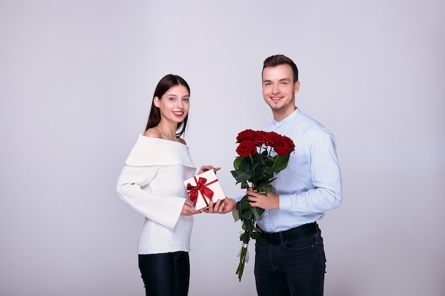 Elegant guy smiles, giving his beautiful womanfriend roses and a gift.