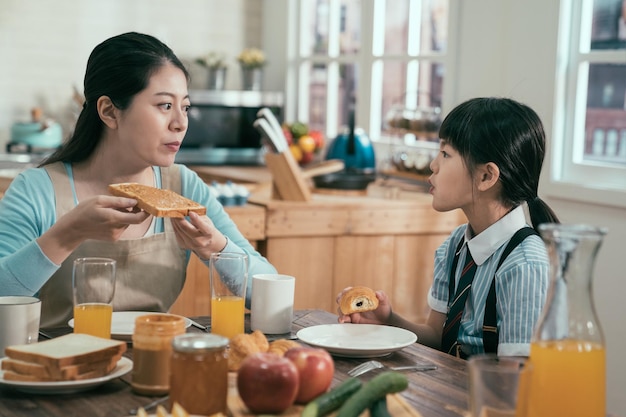 Elegant housewife mother and cute daughter eating togetherness\
cheerful concept. young mom and kid having healthy breakfast after\
dad leaving home going work. parent enjoy morning time with\
child.