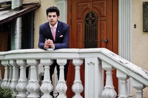 Elegant indian macho man model on suit and pink tie leaned on the railing