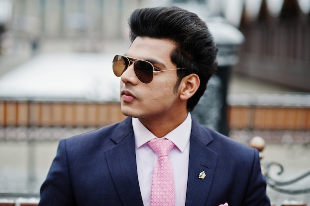 Elegant indian macho man model on suit and pink tie, sunglasses posed on winter day and sitting on bench.