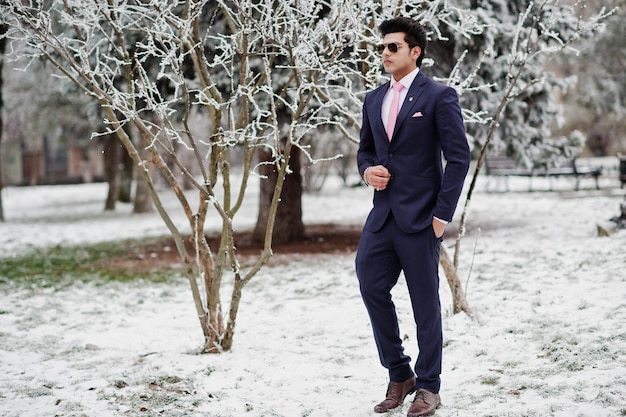 冬の日にポーズをとったスーツとピンクのネクタイサングラスのエレガントなインドのマッチョな男モデル