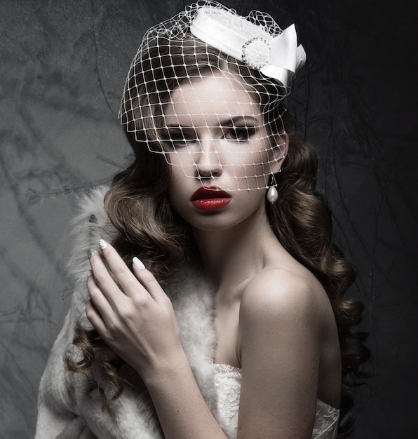 Elegant lady in fur coat with veil and nail Design. Winter image. Picture taken in the studio on a gray background. Beauty face.