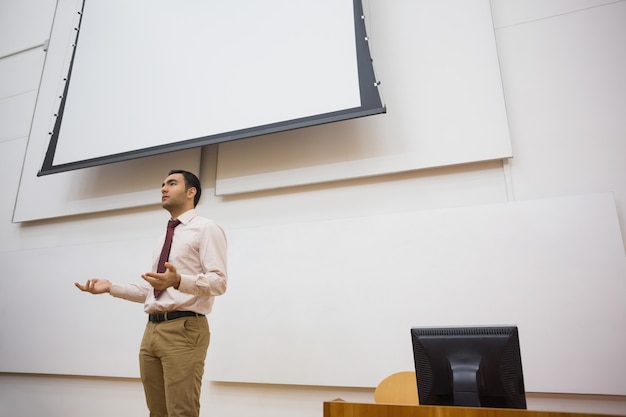 Foto insegnante maschio elegante che sta contro lo schermo di proiezione nell'aula magna