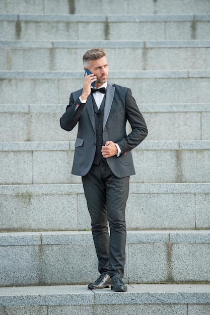 Elegant man in bowtie suit outdoor businessman man using phone man boss speak on smartphone